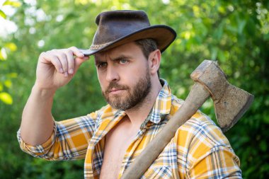 Elinde balta olan kovboyun yüzü. Baltalı kovboy kareli gömlek giyiyor. Dışarıda baltası olan bir kovboy. Kovboyun baltalı fotoğrafı..