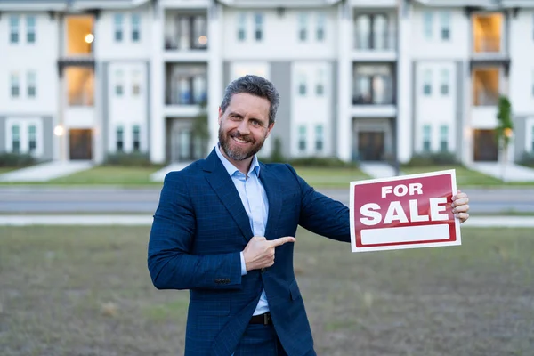 photo of broker with for sale board, point finger. sale property by broker. man broker hold board for sale property. sale property by broker outdoor.
