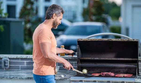 stock image man preparing grilled food at backyard barbecue. man with hot grill at a barbecue party. Expert grill chef. man grilling delicious barbecue on a summer day.