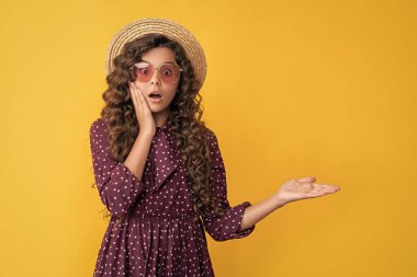 Hasır şapkalı, güneş gözlüklü, uzun esmer kıvırcık saçlı çocuk ürününü sunuyor..