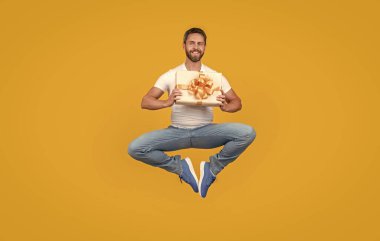 Teslimatçı elinde hediye kutusuyla havada süzülüyor. Şu anki sarı arka planı olan mutlu bir adam. Teslimat servisi. Hediye ve hediye teslimi.