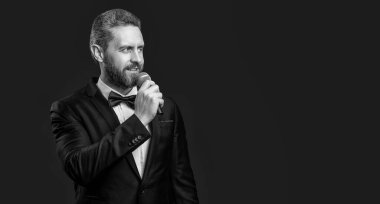 Smokinli sunucunun fotoğrafı. Mikrofon, fotokopi odası. Smokin sunucusu kırmızı arka planda izole edilmiş. Stüdyoda sunucu. Mikrofonlu smokin adam sunucusu.