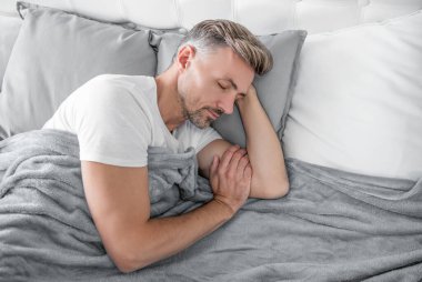 Olgun adam yatakta kestirir. Sabah erken saatlerde.