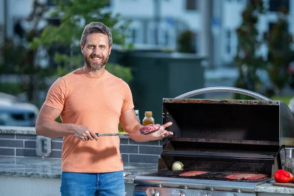 Stock image man with hot grill at a barbecue party. man grilling delicious barbecue on a summer day. Mouthwatering barbecue feast. man preparing grilled food at backyard barbecue.