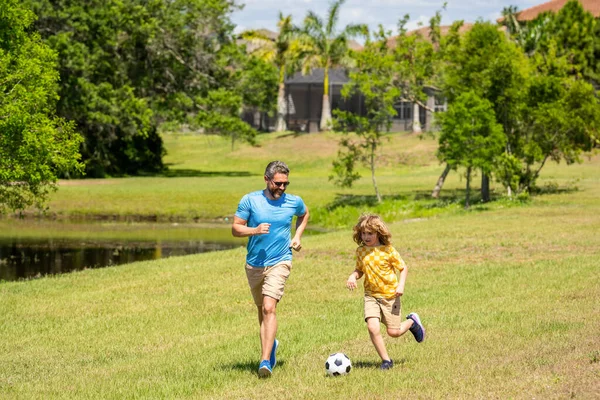 Father dad and son enjoy outdoor activities together. Outdoor adventures between father and son. Active father son playing football in summer. Father and child son teaming up outdoor. football pitch.