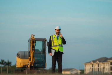 Mimar işgali adamı telefonda konuşuyor. Mimarların adamı açık havada çalışıyor. Mimar işgali mühendisi kask takıyor. Mimarlık mesleğinin fotoğrafı..