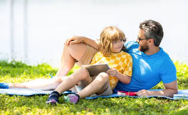 family education of father and son kid. Father shapes son education with book and tablet. Father and son relax in park. childhood school education. son with father bonding in summer. books outdoors.