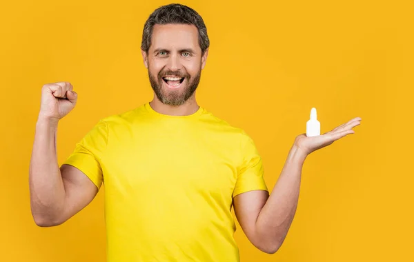 stock image happy man with nasal medicine in studio. photo of man with nasal medicine drops. man with nasal medicine isolated on yellow. man with nasal medicine on background.