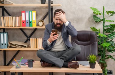 Hayır, olamaz. Stresli iş adamı mesajları okur. İş stresinden panik atak. İş yerinde stres. Masanın üzerinde bağdaş kurarak oturuyor. Panik içinde kıvranan kafa.
