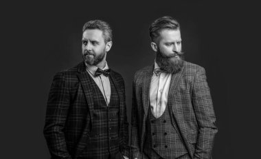 Papyonlu yakışıklı smokinli adamlar, bordo arka planda izole edilmiş. Smokin papyonlu iki adam. Papyon ve smokin giyen adamların stüdyo fotoğrafları. Takım elbiseli, papyonlu şık adamlar..