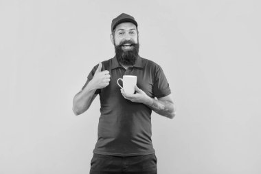 Kırmızı şapkalı ve tişörtlü mutlu sakallı adam başparmağında bardak sarısı arka plan, kahve....