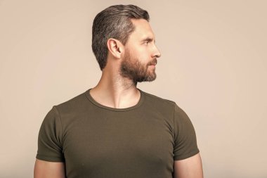 Beyaz adamın sakallı yüzünün profil fotoğrafı. Kirli sakallı beyaz adam tişört giyiyor. Gri arka planda sakallı beyaz bir adam var. Stüdyoda sakalı olan beyaz bir adam..