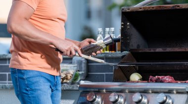 Dışarıdaki adam ızgara ve barbekü tabakları pişiriyor. Dumanlı barbeküde ızgara yapan adam. Izgara maşaları hazır. Izgaracı adam barbeküde et pişiriyor..
