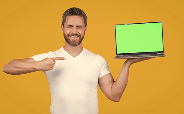 スタジオで携帯用ノートパソコンを提示する男 指を指す 携帯用ノートパソコンを見せてる 携帯型ノートパソコンの画面をコピースペースで提示する男 黄色で隔離されたポータブルノートパソコンを見せる男 — ストック写真