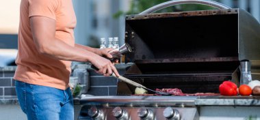 Izgaracı adam barbeküde et pişiriyor. Dışarıdaki adam ızgara ve barbekü tabakları pişiriyor. Sosyetik ızgara uzmanıyım. Dumanlı barbeküde ızgara yapan adam. onglet bifteği.