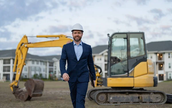 photo of positive businessman with building plan wearing hardhat. businessman with building plan. businessman check building plan at site. businessman checking building plan outdoor.