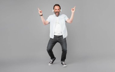 Mutlu eski rockçı rock müzik eşliğinde şarkı söyler kulaklıkla çalar boynuz işaretleri gri arka plan, şarkı.