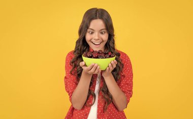 amazed girl hold cherry bowl on yellow background.