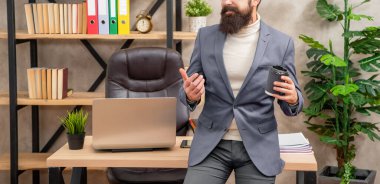 Profesyonel bir adam elinde çay ya da kahve fincanı tutarken ofis masasına oturur, mola verir..