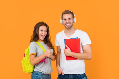 Sarı arka planda çalışma kitabı ve sırt çantasıyla mutlu iki öğrenci baş parmağını kaldırdı ve eğitime başladı..
