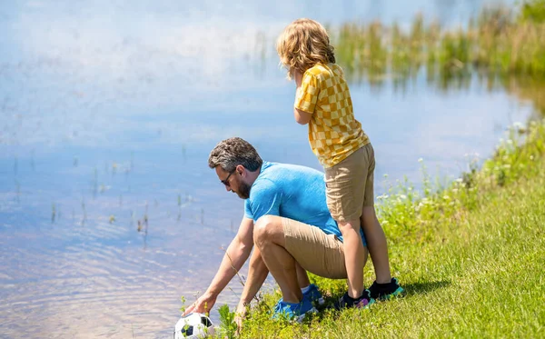 Father trainer and child son teaming up outdoor. Father dad and son enjoying outdoor activities together. Outdoor adventures between father and son. Active father son playing football in summer.