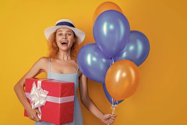 laughing birthday woman with present in studio. birthday woman with present on background. photo of birthday woman with present and balloons. birthday woman with present isolated on yellow.