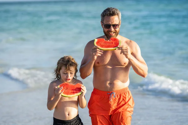 happy dad with son child childhood at the beach. Loving father dad and son childhood enjoying quality time together at sea. dad and son eating watermelon. dad father and son on summer vacation.