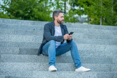 Dışarıdaki telefondan erkek mesajlaşması. Sokakta telefonla mesajlaşan bir adam. Adam dışarıda telefonla mesajlaşıyor. Ellerinde telefonla mesajlaşan adamın fotoğrafı..