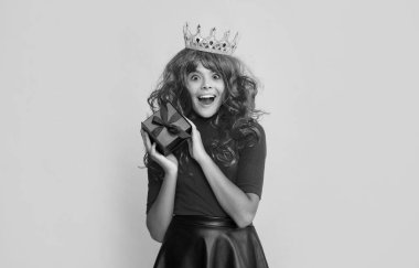 Sarı arka planda hediye kutusuyla prenses tacındaki hayrete düşmüş çocuk..