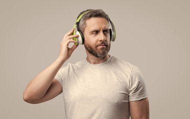 Yakışıklı adam stüdyoda kulaklıkla müzik dinliyor. Adam modern kulaklıkla müzik dinliyor. Kulaklıkla müzik dinleyen bir adamın fotoğrafı. Adam kulaklıkla müzik dinliyor. Gri arka planda izole edilmiş..