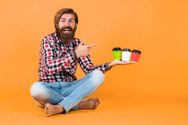 Kareli gömlekli, modaya uygun saç stili olan beyaz, olgun bir hippi sabah kahvesini kağıt bardaktan, sıcak içecekten seçer..