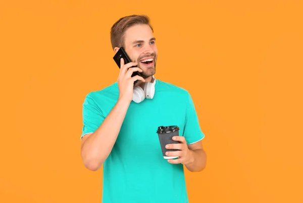 穿着蓝色衬衫的快乐男人在智能手机上说话 早上喝着黄色背景的咖啡 — 图库照片