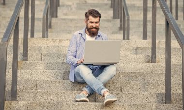 Gülümseyen adamın merdivenlerde otururken çevrimiçi video bağlantısı var. Adamın bilgisayarında çevrimiçi video bağlantısı var. Adamın dışarıda online video iletişimi var. Adamın dışarıda internet bağlantısı var..
