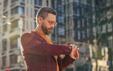 Dakik adamın fotoğrafı. Elle kontrol zamanı. Dışarıda ceketli dakik bir adam var. Dakik adam caddede zamanı kontrol ediyor. Dakik adam dışarıda zamanı kontrol et.