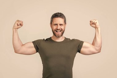 Sakallı, güçlü, kaslı bir adamın fotoğrafı. Güçlü kaslı adam tişört giyer. Gri arka planda izole edilmiş güçlü kaslı adam. Stüdyoda güçlü kaslı adam.