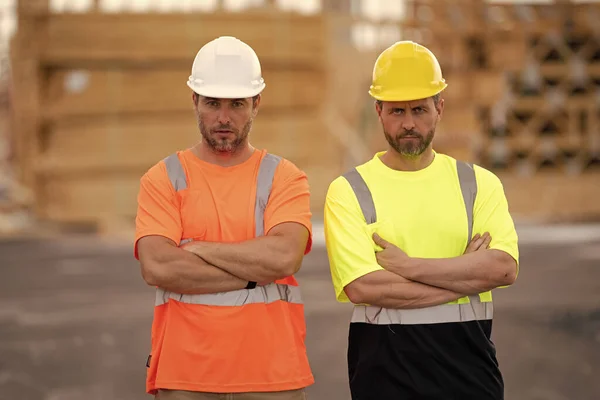 stock image Construction workers at construction site. Serious men wearing safety vests and construction helmets. Construction foreman and builder. Civil engineers keeping arms crossed.