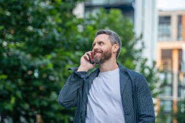 Sokakta akıllı telefon görüşmesi yapan mutlu bir adam. Adam dışarıdaki akıllı telefondan arıyor. Adamın fotoğrafı. Akıllı telefondan ara ve konuş. Adamın açık havada akıllı telefonu var..