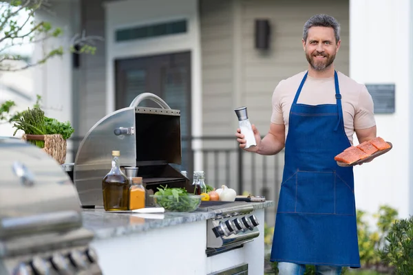stock image barbecue man with salmon in apron, advertisement. photo of barbecue man with salmon fish. barbecue man with salmon. barbecue man with salmon outdoor.