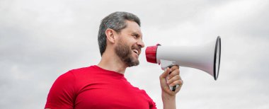 man advertiser in red shirt shout in loudspeaker on sky background.