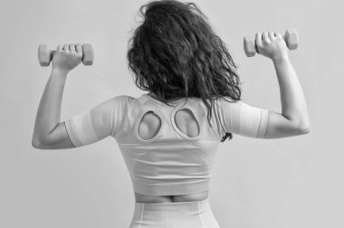 Fitness kadını halter egzersizi yapıyor, halterle, arka görüşle. Fitness kadınları halter egzersizlerini sarı arka planda izole ederler. fitness ve spor.