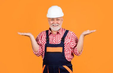 happy old aged man builder in helmet on yellow background.