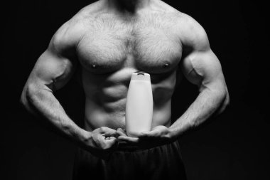 Erkek kozmetik ürünleri olan kaslı adam siyah arka planda izole edilmiş. Stüdyoda kozmetik ürünleri satan kaslı bir adam. Güçlü kaslı adam kozmetik ürünlerini elinde tutuyor. Erkek makyaj şampuanıyla kaslı bir adamın fotoğrafı..