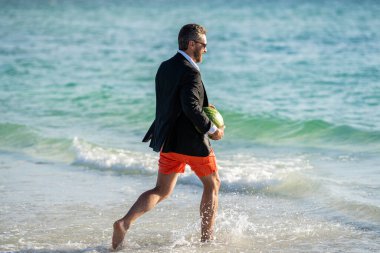 Yaz iş hayalleri. İş adamı tatilde. Denizde karpuz taşıyan takım elbiseli bir iş adamı. Yaz tatilindeki iş adamı. Kumsalda dalgıç kıyafetli bir iş adamı. Yazın iş maceraları.
