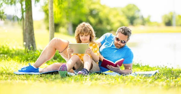 Father shapes son education with book and tablet. Father and son relax in park. childhood school education. son and father bonding in summer. family education of father and son kid. Outdoor education.