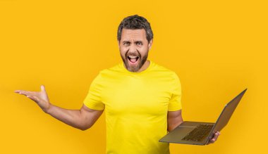 Arka planda stresli bir programcı bağırıyor. Stüdyodaki adam programcı. Dizüstü bilgisayarlı insan programcısının fotoğrafı. Adam programcı sarı üzerine izole.