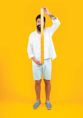 Arka planda cetveli olan neşeli bir adam. Cetvelli bir adamın fotoğrafı. Elinde cetvel olan adam sarıda izole edilmiş. Stüdyoda ölçücü cetveli olan adam.