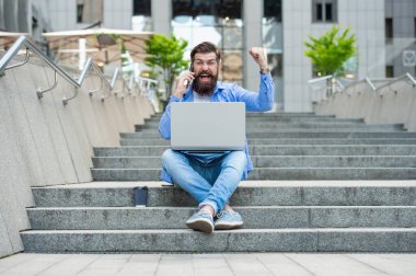 Mutlu adam cep telefonunda bağırarak kazanıyor. Kazanan merdivenlerde oturarak bahsi kazanır. İnternette bahis oynuyorum. Mobil bahis. Kazanmak için bahis.