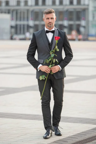 elegant man in black tux. man wearing tux bowtie outdoor. romantic tux man with red rose.