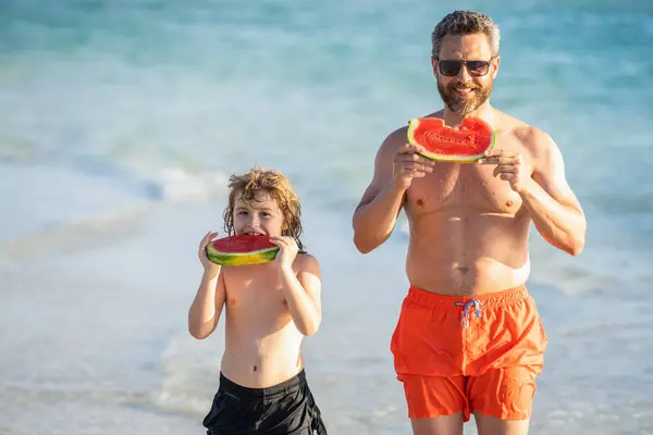 father and son childhood enjoying quality time together at sea. Father dad and son eating watermelon. dad father and son on summer childhood vacation. father with son at the beach.