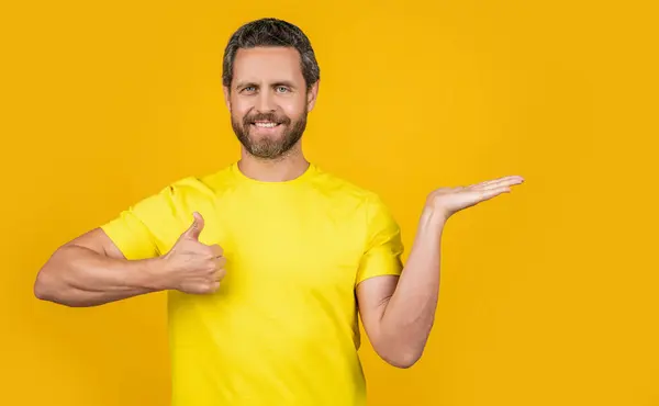 照片上的微笑男子展示广告 大拇指向上 展示黄色广告的人 背景介绍广告的人 在演播室登广告的人 — 图库照片